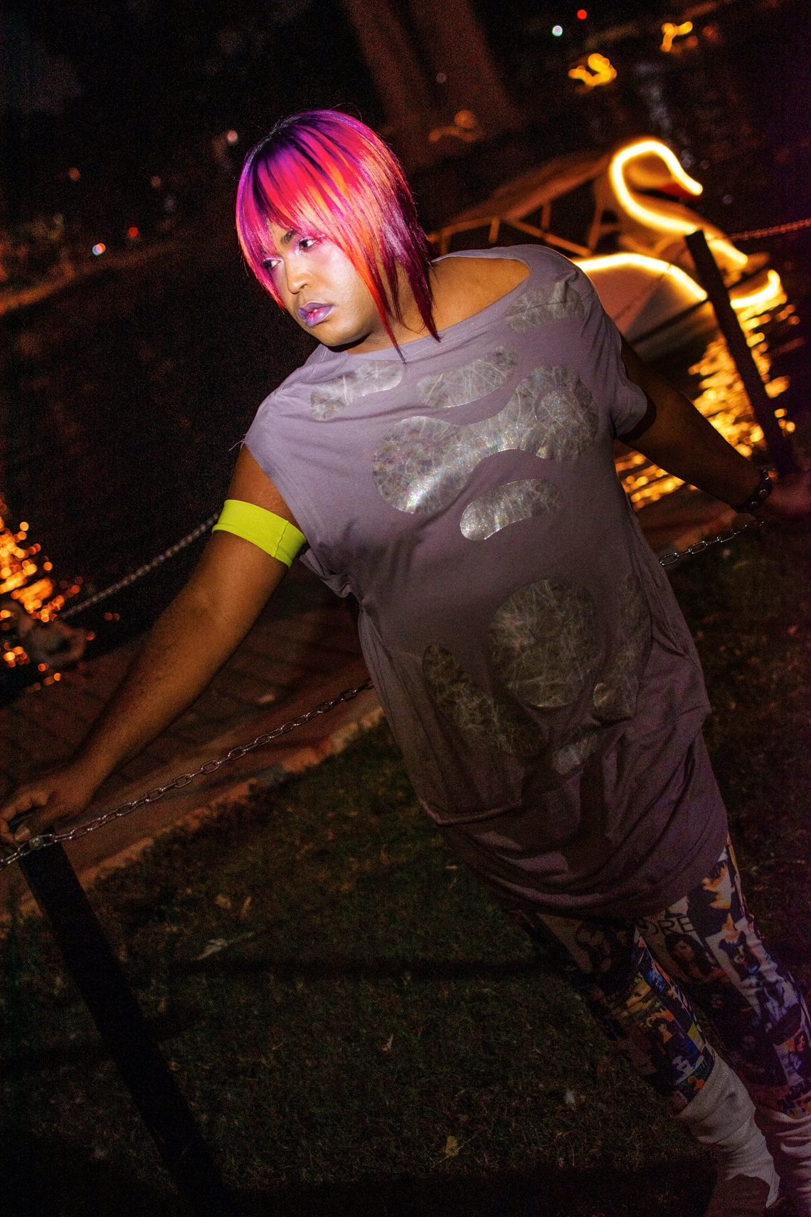 Portrait of DJ Miss Parker looking away from the camera in a park at night with colorful pink hair